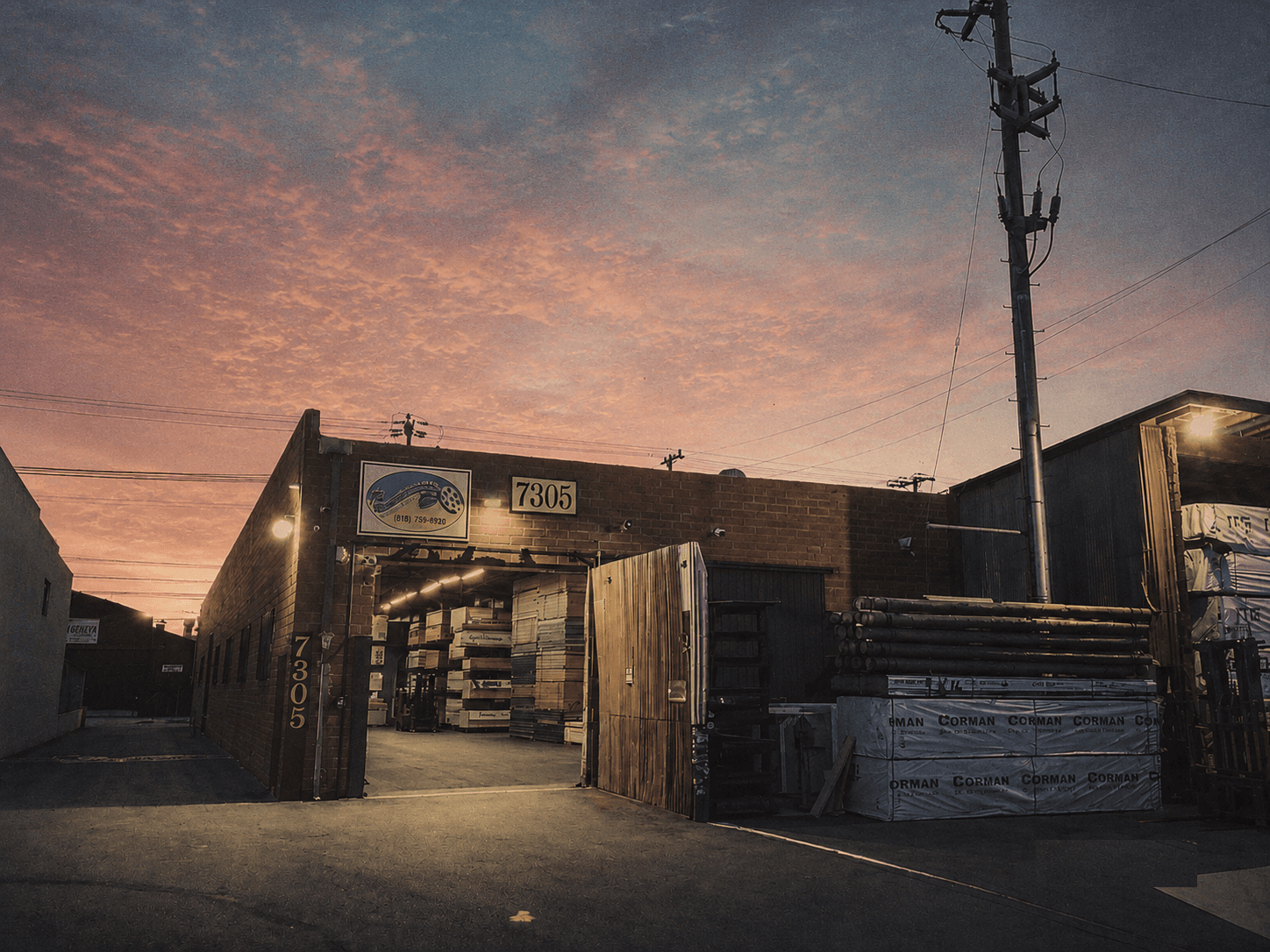The Studio Supply yard at 7305 Ethel Ave at dusk, stacked with lumber and materials